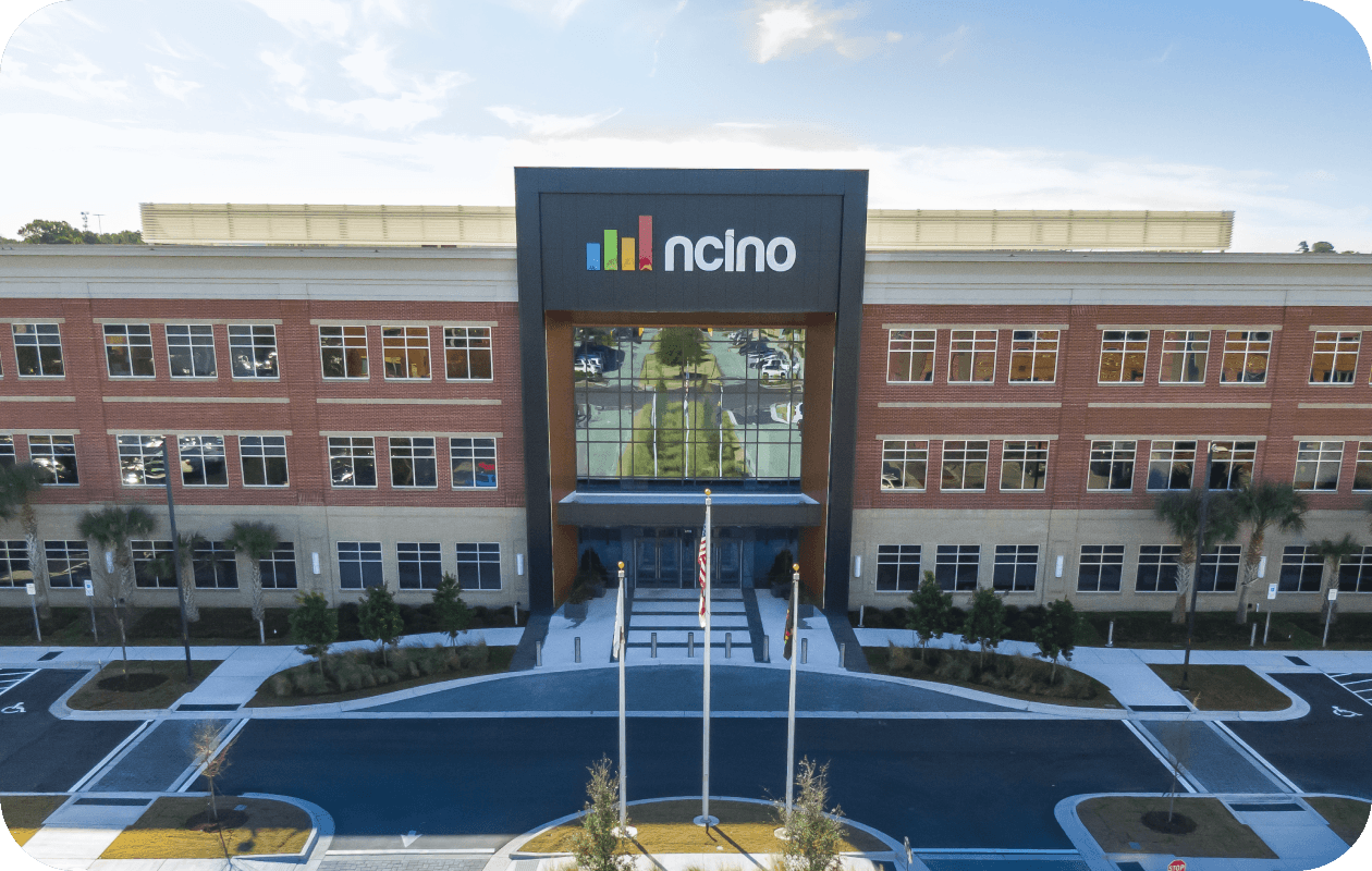 The external view of the nCino building is a brick and concrete building with a large black sign over its entrance surrounded by a parking lot.