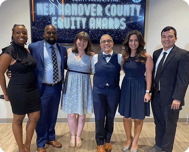 A diverse group of people pose together in front of the New Hanover County Equity Awards sign.