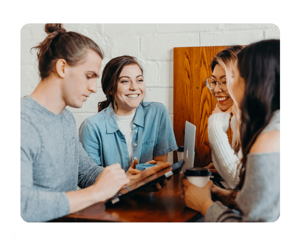 A group of colleagues sitting a round a table chat while they work on a project together.
